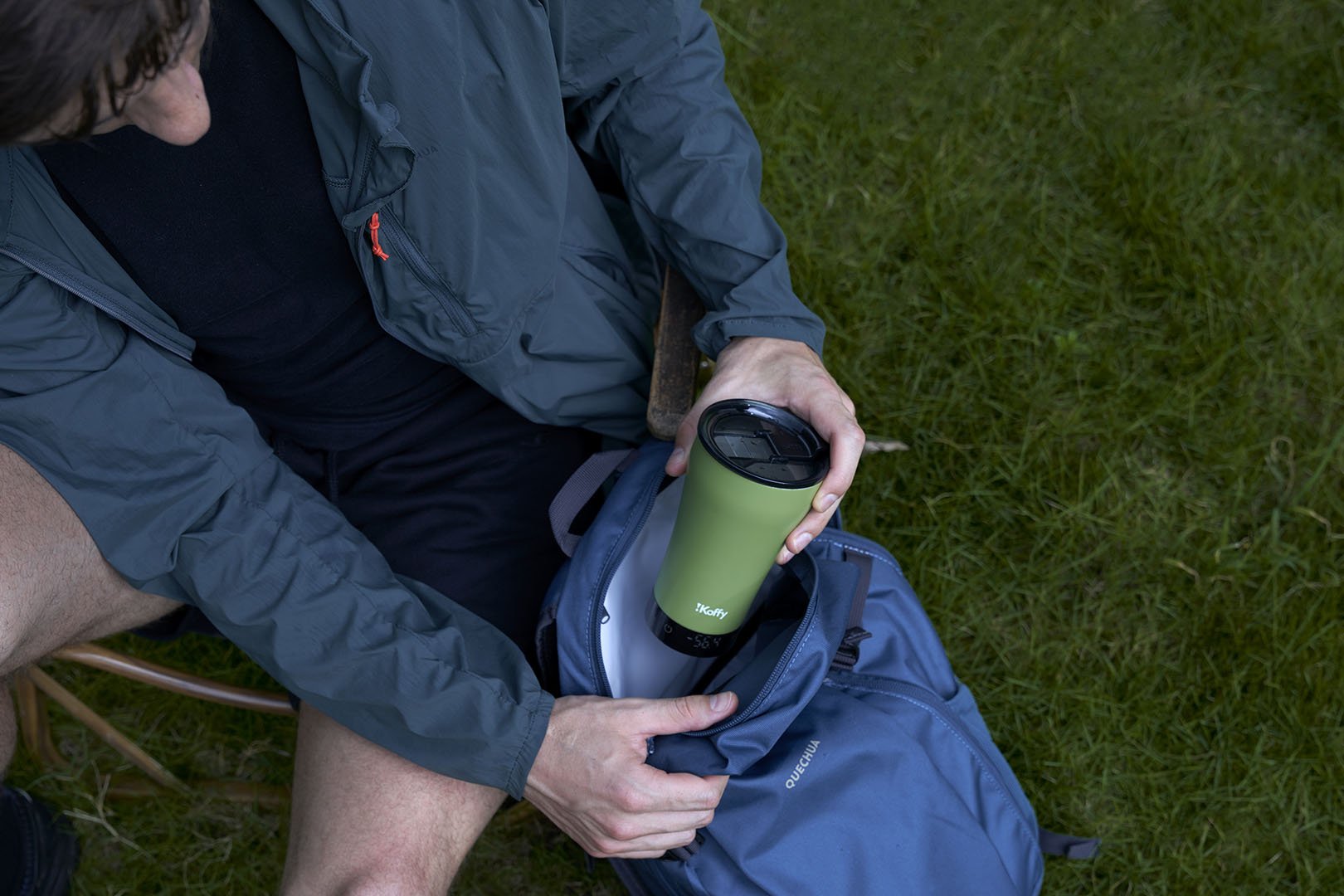 A camper sitting on the grass, packing the iKoffy GoBrew into their backpack, ready for an outdoor coffee adventure.