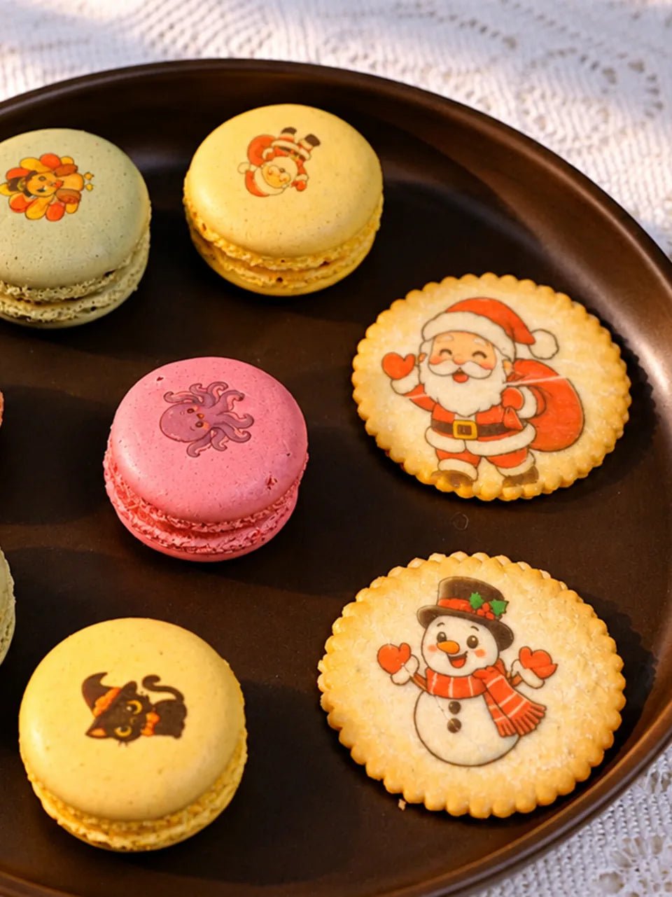 Colorful macarons with printed character designs, served beside decorated cookies.