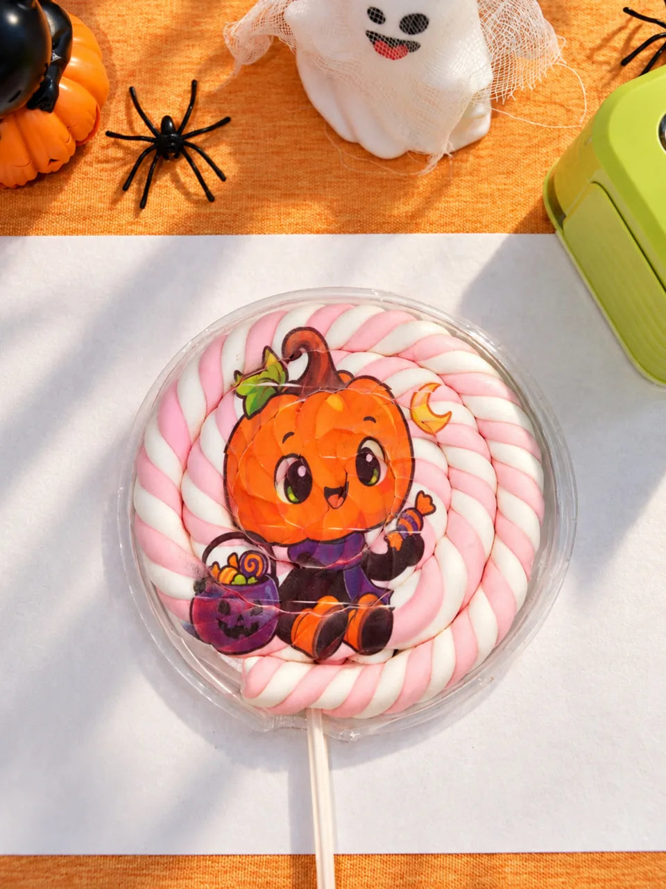 A pumpkin character on a pink-and-white marshmallow lollipop.