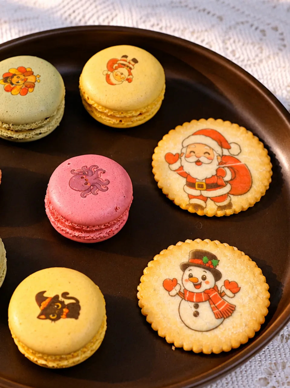 Colorful macarons with printed character designs, served beside decorated cookies.